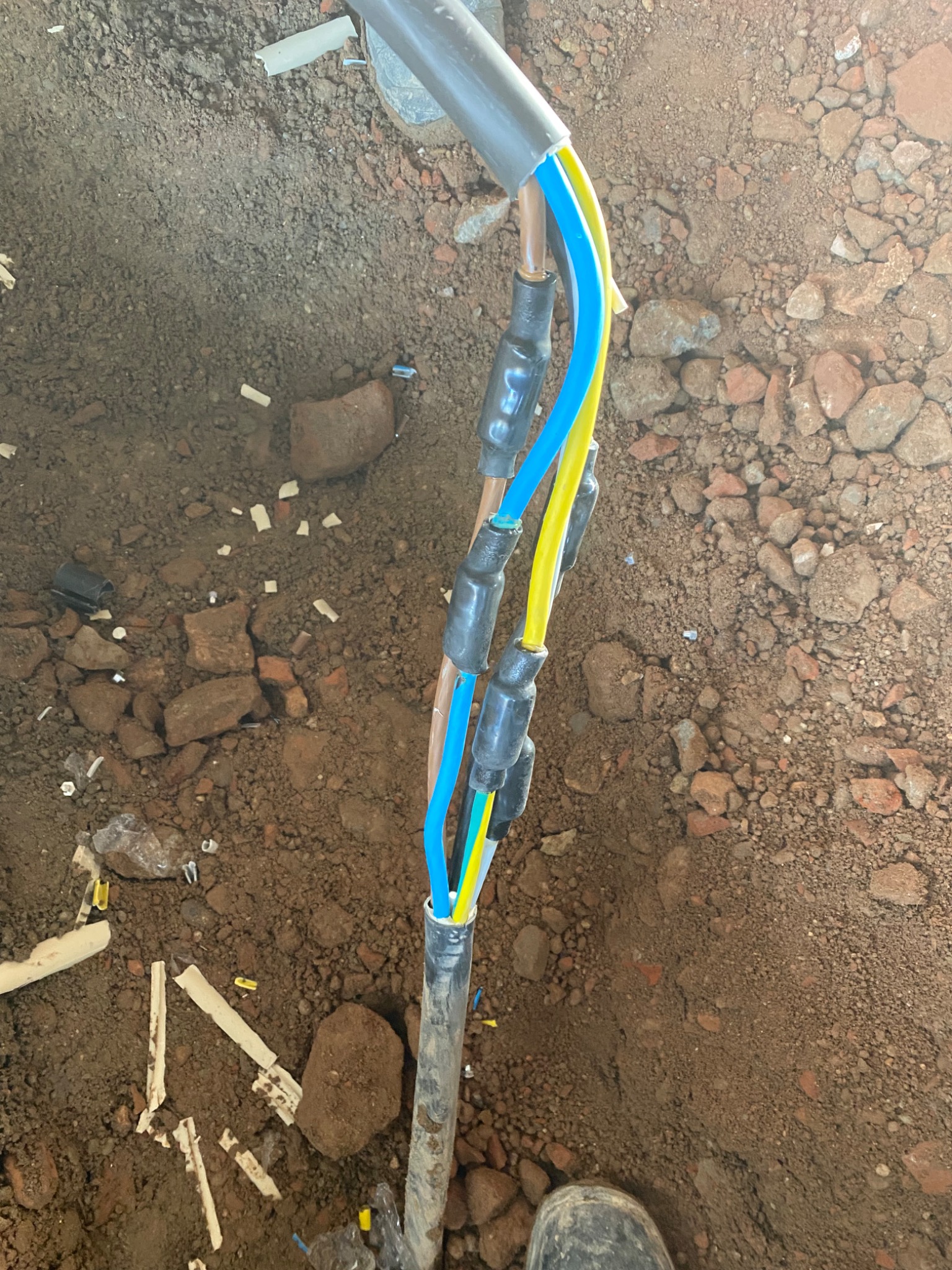 Wykop z ziemią i gruzem, w którym widoczne są zabezpieczone złączki kabli elektrycznych w Zdzieszowicach, wychodzące z rury PCV.