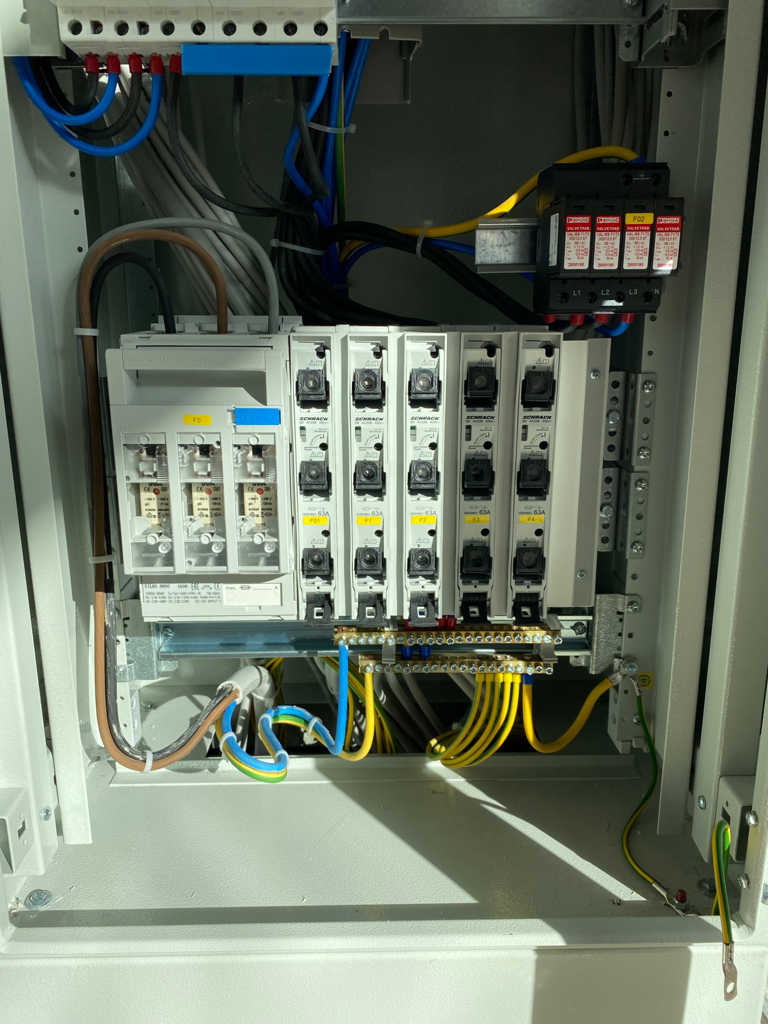 Otwarta skrzynka rozdzielcza z zainstalowanymi bezpiecznikami, warystorami i okablowaniem, widok z bliska, wewnątrz budynku.