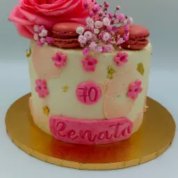 Tort urodzinowy dla Renaty na 70 urodziny, zdobiony różową różą, makaronikami i gipsówką, na złotym podkładzie.