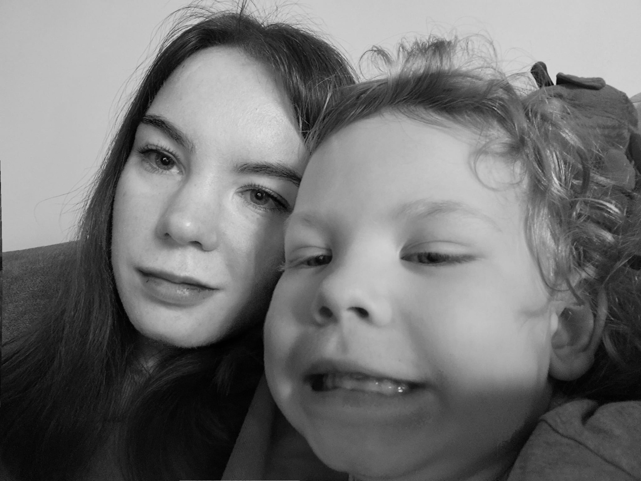 Czarno-białe zbliżenie kobiety i dziecka z kręconymi włosami, uśmiechające się do kamery, z widocznymi detalami twarzy i włosów.