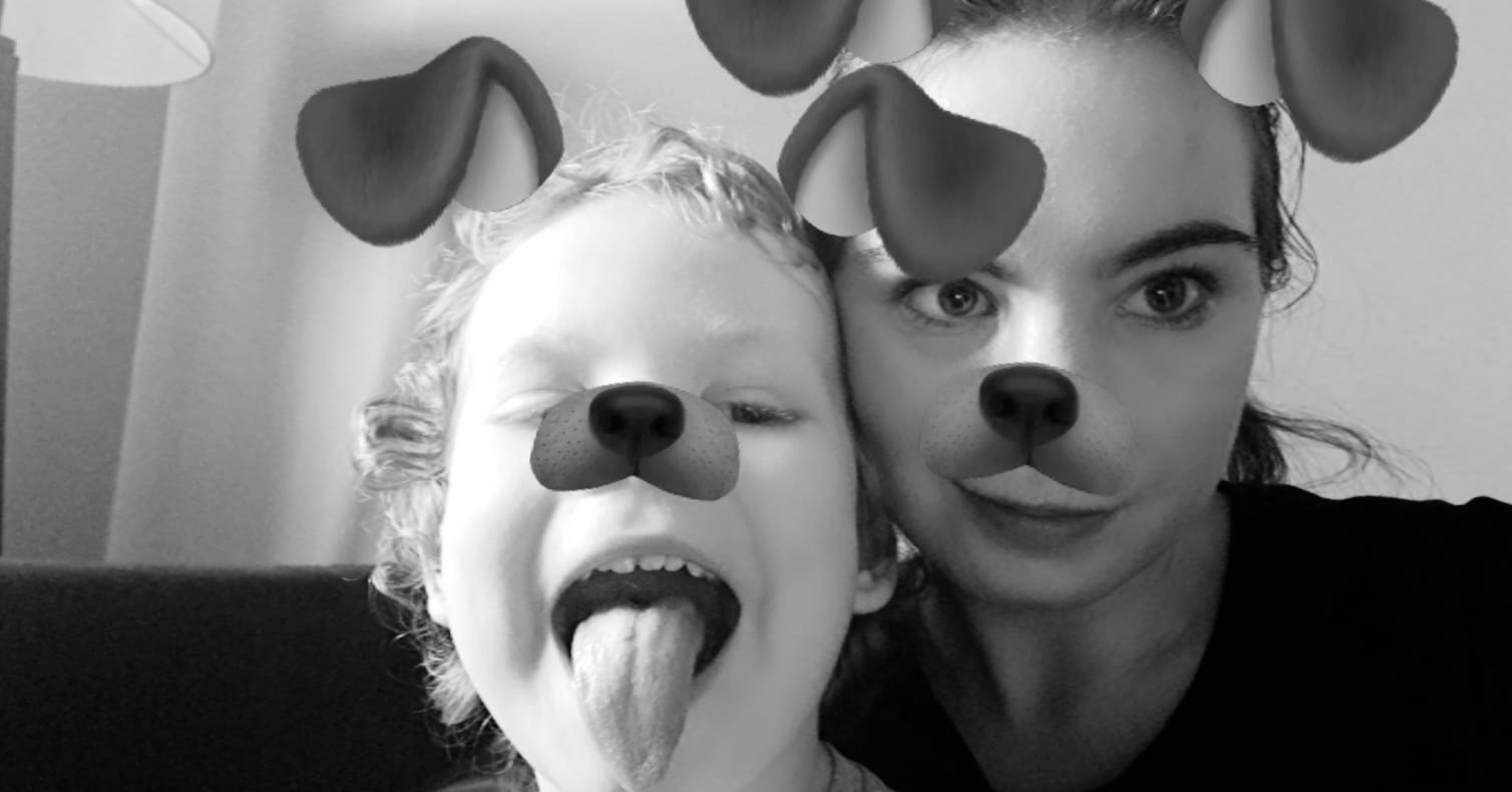 Czarno-białe selfie kobiety i dziecka z filtrami psimi uszami i nosami, dziecko z wyciągniętym językiem i przymkniętym okiem.