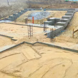 Przygotowanie fundamentów pod budynek z widocznymi zbrojeniami stalowymi i wylanymi betonowymi ławami fundamentowymi, teren wyrównany piaskiem.