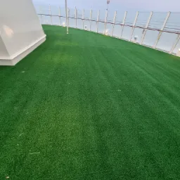 Zielony taras z syntetycznej trawy na statku lub budynku z przeszkloną balustradą i zadaszeniem, widok z dołu.