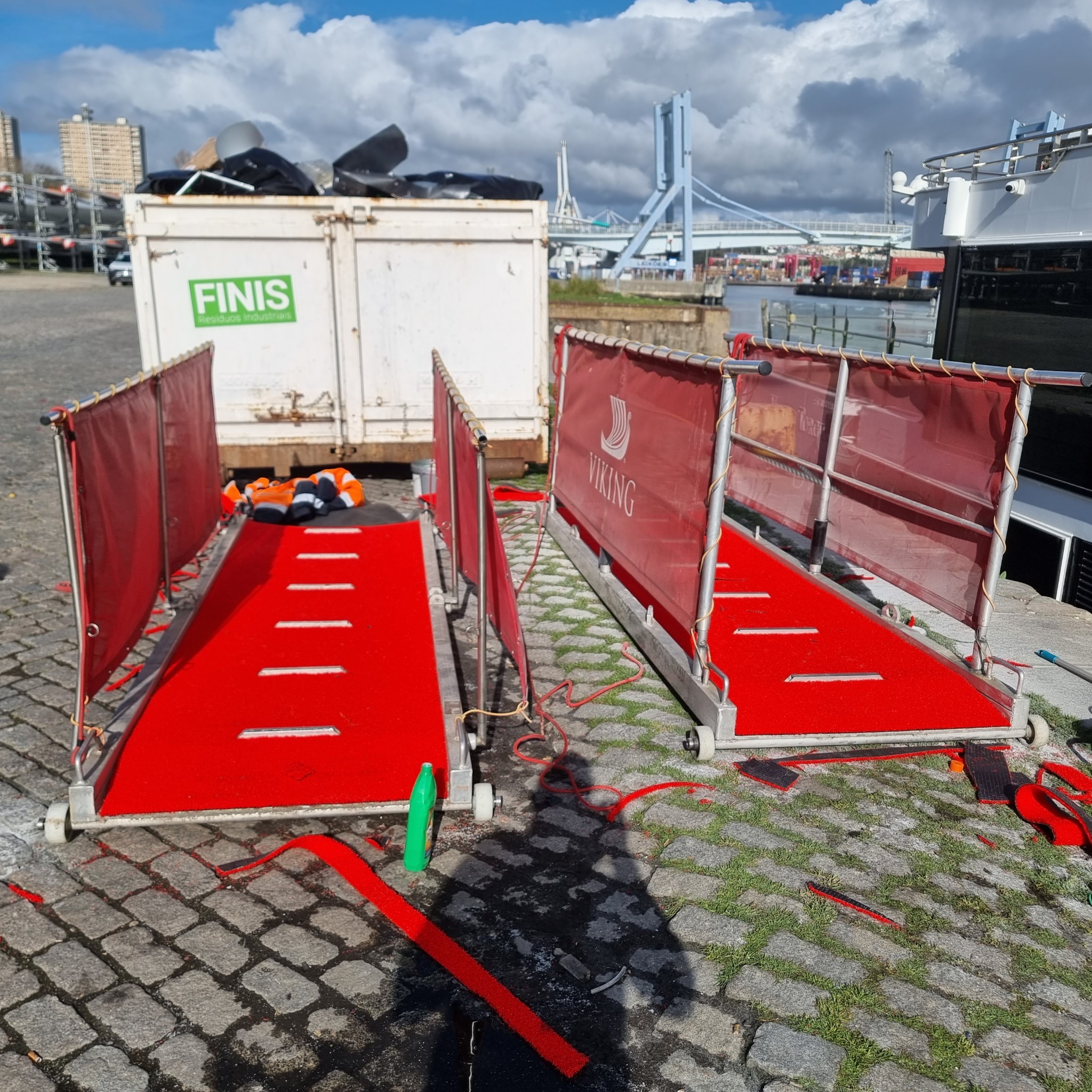 Dwa czerwone chodniki z metalową ramą i czerwonymi panelami bocznymi z logo Viking, stojące na brukowanej powierzchni, z kontenerem na śmieci i budynkami w tle.