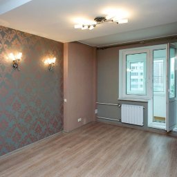 Serhii Cholavyn - Pusty pokój po remoncie z wzorzystą tapetą w odcieniach szarości i miedzi, panelami podłogowymi imitującymi drewno, grzejnikiem pod oknem i nowoczesnym oświetleniem sufitowym oraz kinkietami...