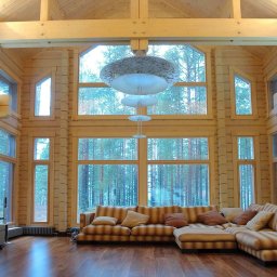 Serhii Cholavyn - Wnętrze domu z bali z dużymi oknami z widokiem na las, drewniana podłoga i sofa w paski, oświetlenie sufitowe w stylu nowoczesnym.
