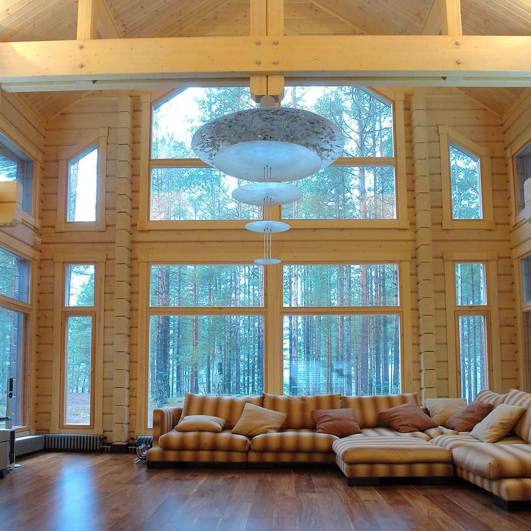 Wnętrze domu z bali z dużymi oknami z widokiem na las, drewniana podłoga i sofa w paski, oświetlenie sufitowe w stylu nowoczesnym.