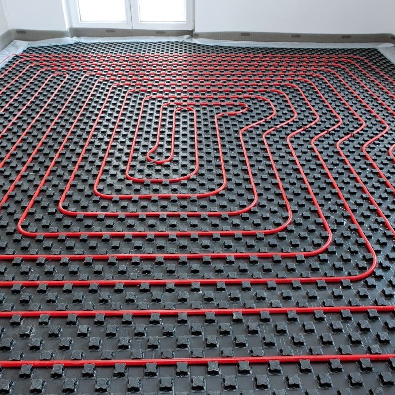 Czerwone rury ogrzewania podłogowego ułożone na czarnej, matowej płycie izolacyjnej z wypustkami, widok z góry, przygotowane do zalania wylewką.
