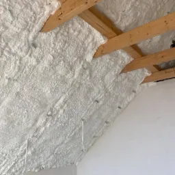 Poddasze ocieplone białą pianką PUR, widoczne drewniane krokwie i wystające białe przewody.