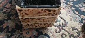 Drewniana skrzynka na kwiaty z efektem przypalenia, wyłożona czarną folią, stojąca na wzorzystym dywanie.