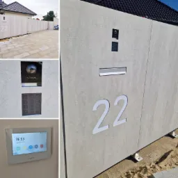 Nowoczesny, jasnoszary panel ogrodzeniowy z numerem domu '22', wideodomofonem z kamerą, klawiaturą numeryczną i skrzynką na listy, uzupełniony o panel sterujący wewnątrz budynku, pokazujący godzinę...