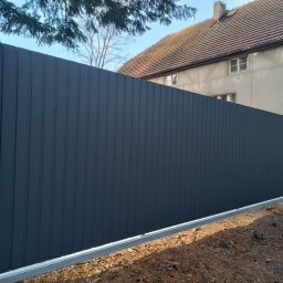 Ur-Stal Waldemar Urbaniak - Nowoczesna brama przesuwna z ciemnoszarej blachy trapezowej, osadzona na betonowych słupkach z dekoracyjnym wzorem, widok z zewnątrz.