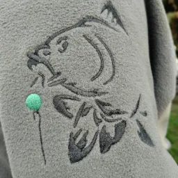 Szara bluza polarowa z haftowanym motywem ryby (karp) i zieloną kulką na nitce, detale haftu.