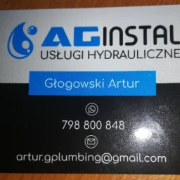 Wizytówka firmy AG Instal Usługi Hydrauliczne z logo przedstawiającym kroplę wody, numerem telefonu i adresem email, leżąca na drewnianym blacie.