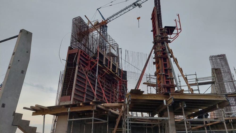 Konstrukcja zbrojeniowa z szalunkiem podczas budowy budynku, widoczny żuraw budowlany na tle pochmurnego nieba.