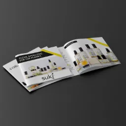 Otwarty katalog produktowy marki kosmetyków naturalnych Suki, prezentujący serię produktów w minimalistycznych opakowaniach na białym tle, z żółtymi akcentami, leżący na ciemnoszarym tle.