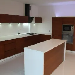 Nowoczesna kuchnia z drewnianymi frontami szafek, białym blatem i wyspą kuchenną, oświetleniem punktowym podszafkowym i wbudowanym piekarnikiem z mikrofalówką.