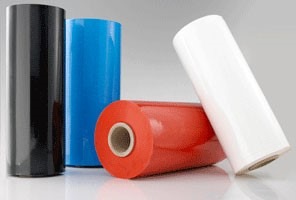 Rolki folii w kolorach: czarnym, niebieskim, czerwonym i białym, ułożone na błyszczącej powierzchni. Widoczne rdzenie rolek.