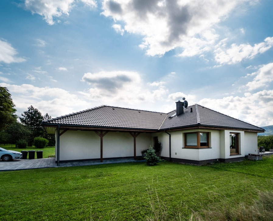 Parterowy dom z kremową elewacją i zadaszonym tarasem, widok z ogrodu w słoneczny dzień.