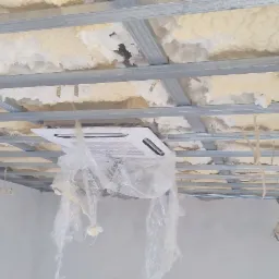 Sufit podwieszany z metalową konstrukcją, ocieplony pianą, z zamontowanym klimatyzatorem zabezpieczonym folią ochronną.