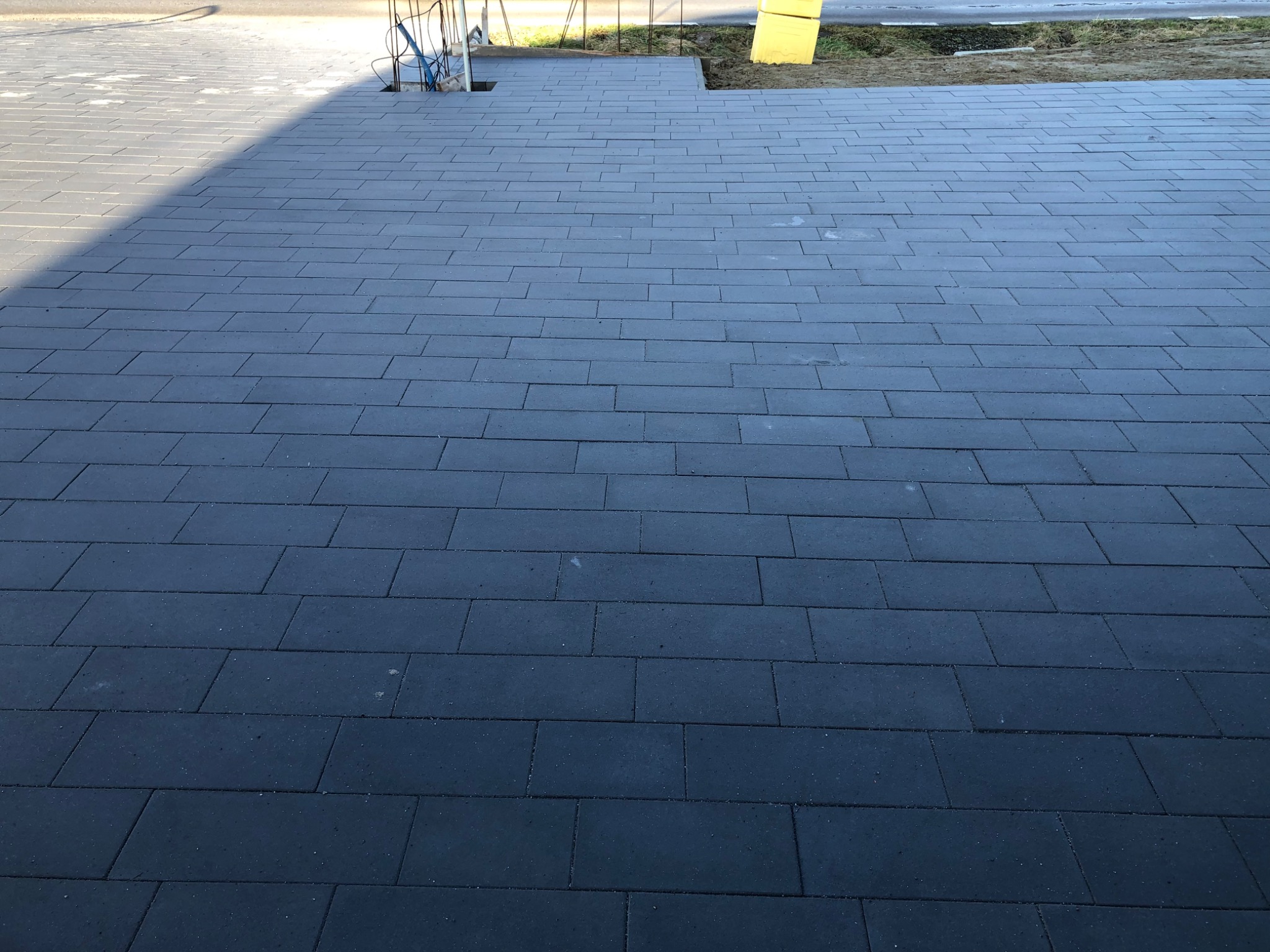 Nowa, ciemnoszara kostka brukowa ułożona na posesji, widoczny fragment chodnika i przygotowane miejsce pod schody.