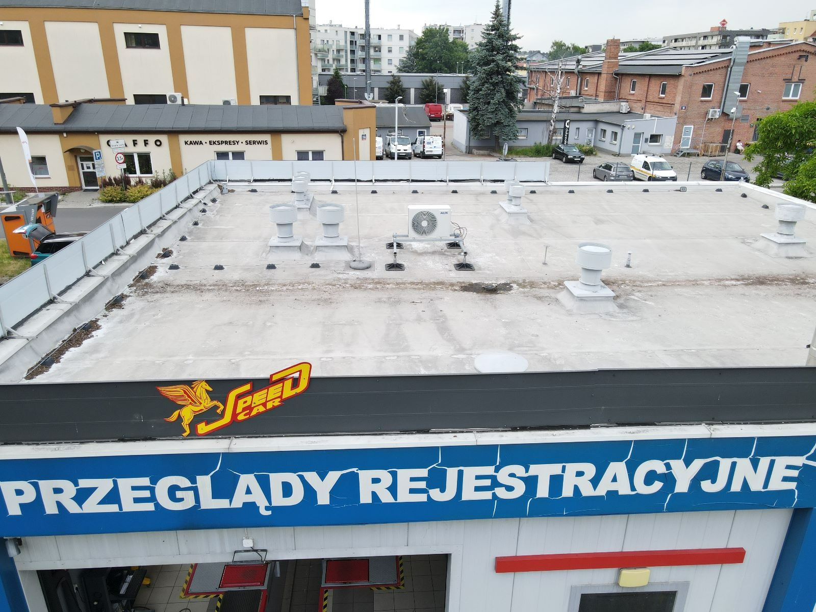 Widok z góry na dach budynku z zamontowaną jednostką zewnętrzną klimatyzacji AUX, kominami wentylacyjnymi i widocznym logo firmy Speed Car.