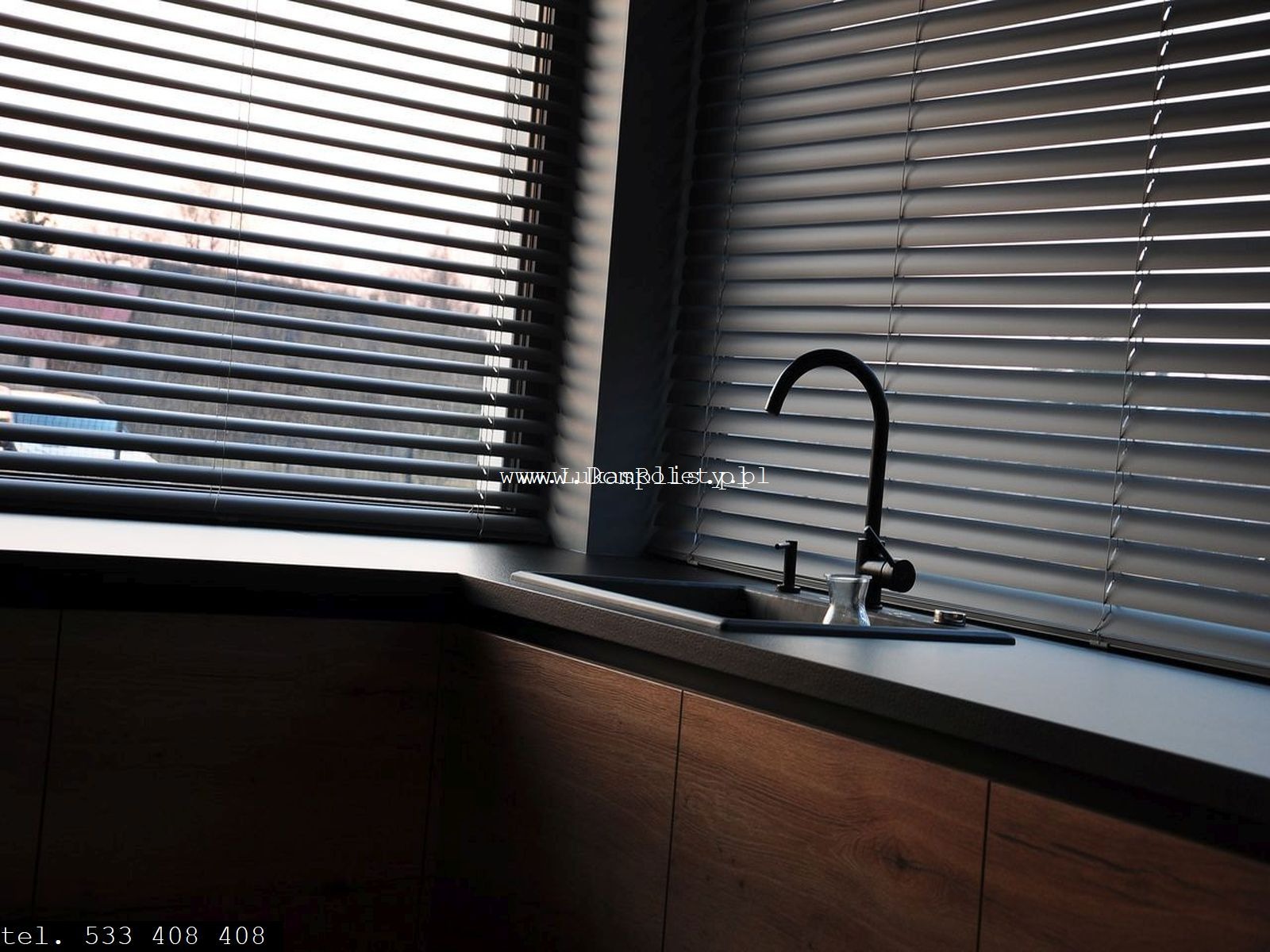 Nowoczesna kuchnia z drewnianymi szafkami, czarnym blatem, minimalistyczną armaturą i żaluzjami poziomymi w oknie, zapewniającymi prywatność.