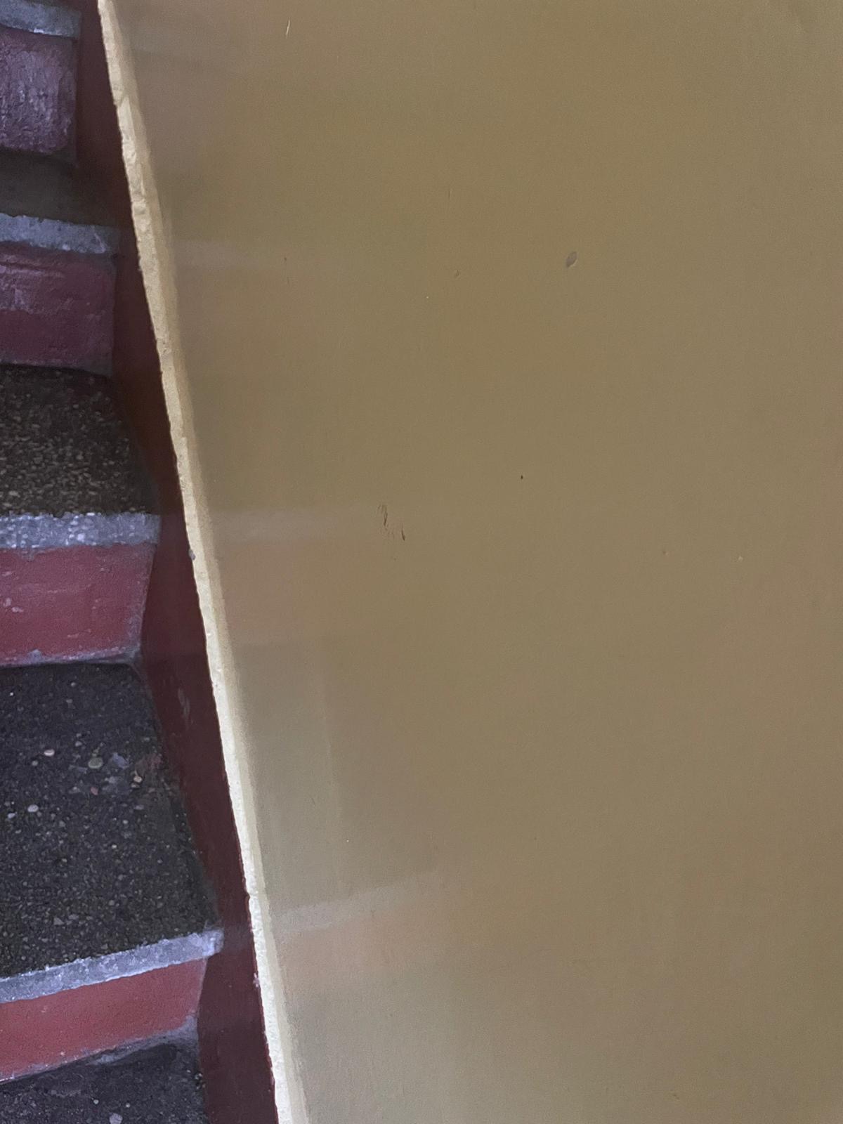 Fragment klatki schodowej we Wrocławiu z widocznymi schodami wyłożonymi czarną, szorstką nawierzchnią i ścianą pomalowaną na beżowo z delikatnymi zabrudzeniami.