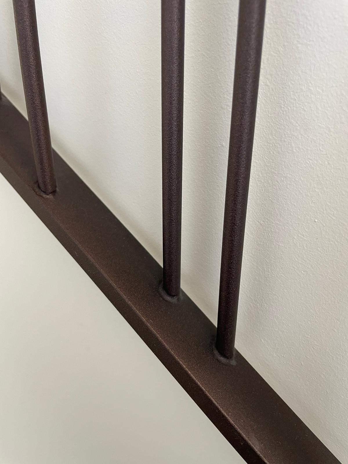 Metalowa balustrada w kolorze ciemnego brązu, przymocowana do białej ściany, widoczny detal spawów.