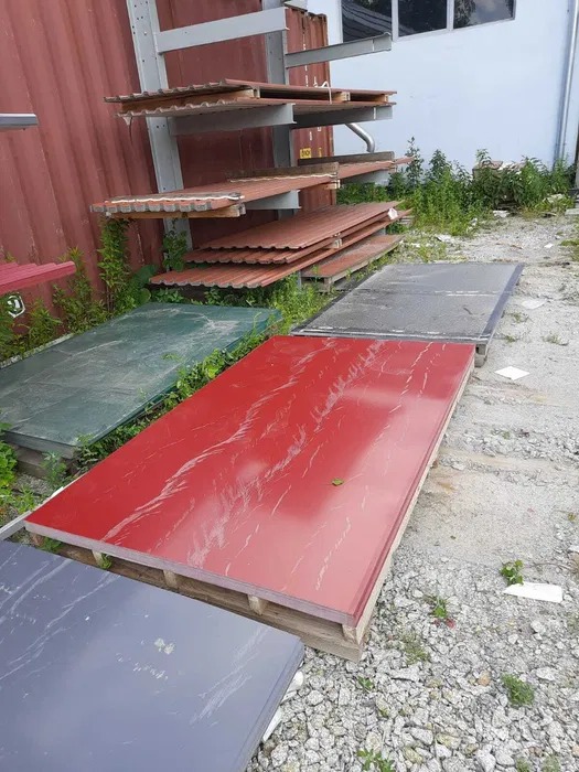 Ekspozycja różnokolorowych arkuszy blachy na paletach i regale, z bliska. Czerwony arkusz z marmurkowym wzorem na pierwszym planie.
