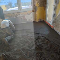 LbM wylewki maszynowe - Pracownik w Cieszynie wyrównuje mokrą wylewkę jastrychową w pomieszczeniu z oknem, przygotowując podłoże pod dalsze prace wykończeniowe.