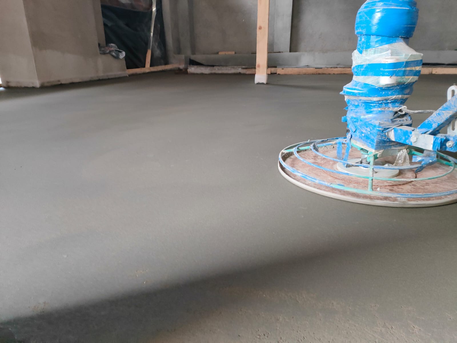 Świeżo wylana, gładka posadzka jastrychowa wygładzana maszyną z niebieską obudową na budowie.