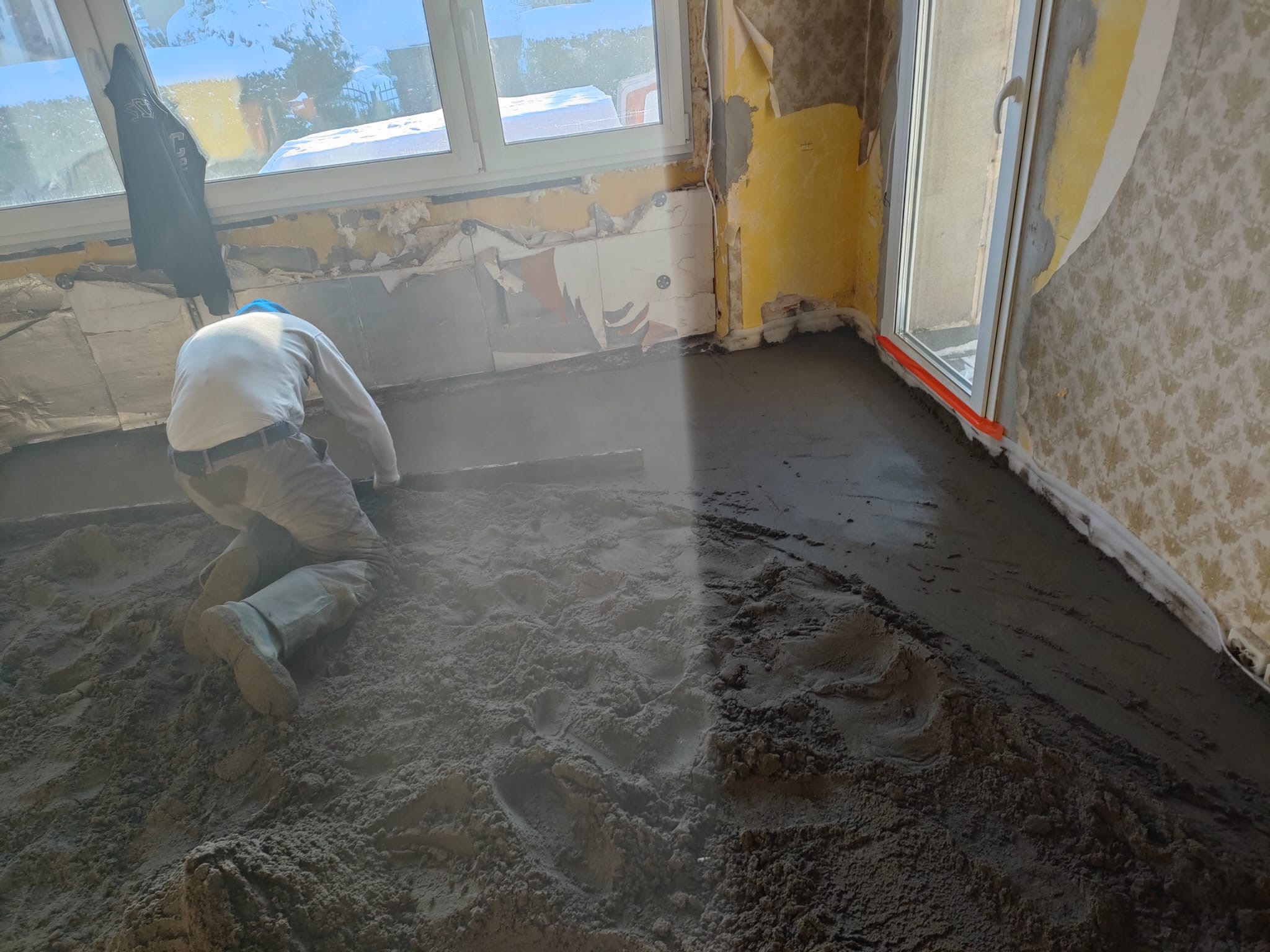 Pracownik w Cieszynie wyrównuje mokrą wylewkę jastrychową w pomieszczeniu z oknem, przygotowując podłoże pod dalsze prace wykończeniowe.