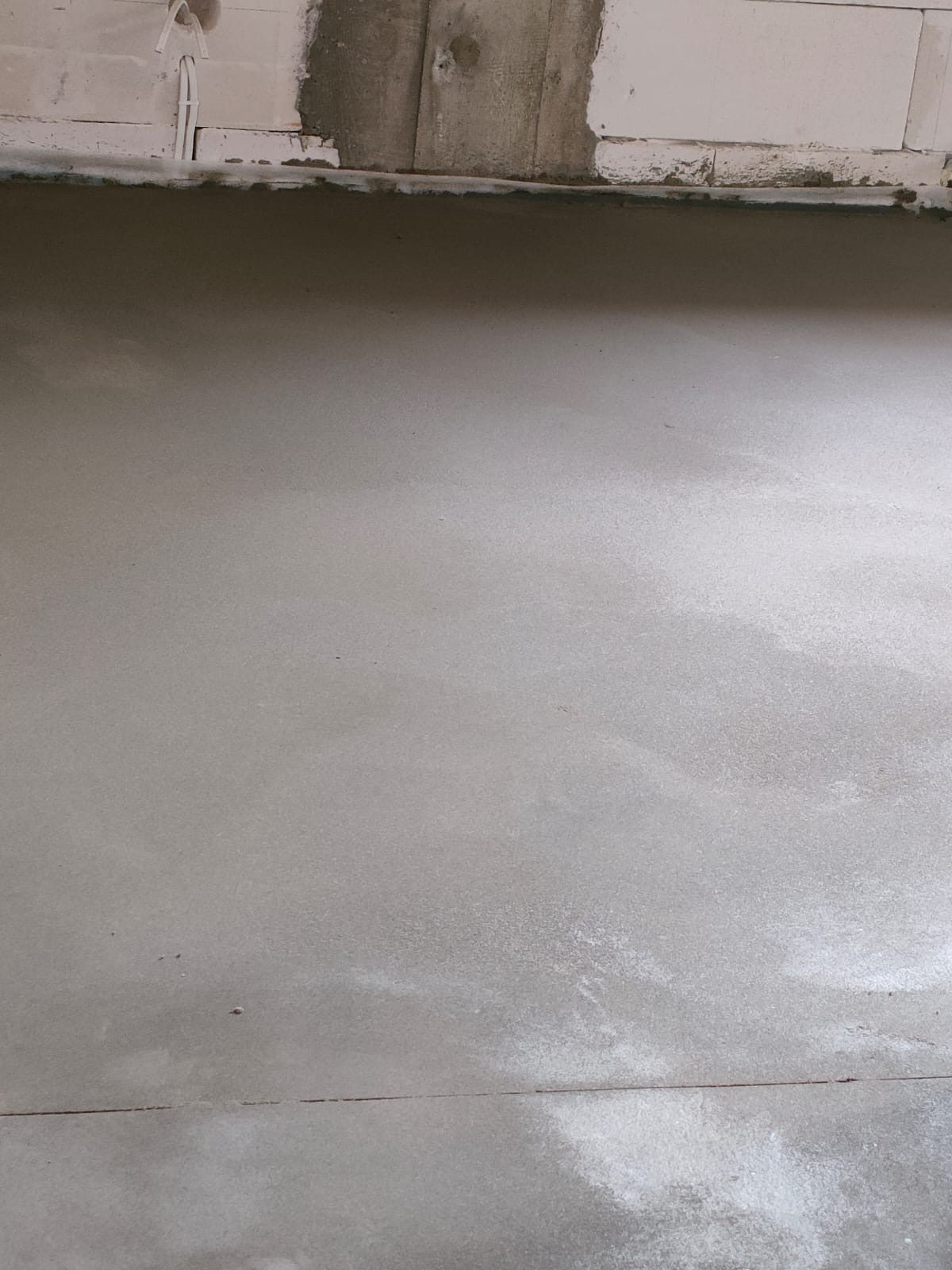 Świeżo wylana, gładka posadzka jastrychowa, widoczne ślady po szlifowaniu przy ścianie z bloczków.