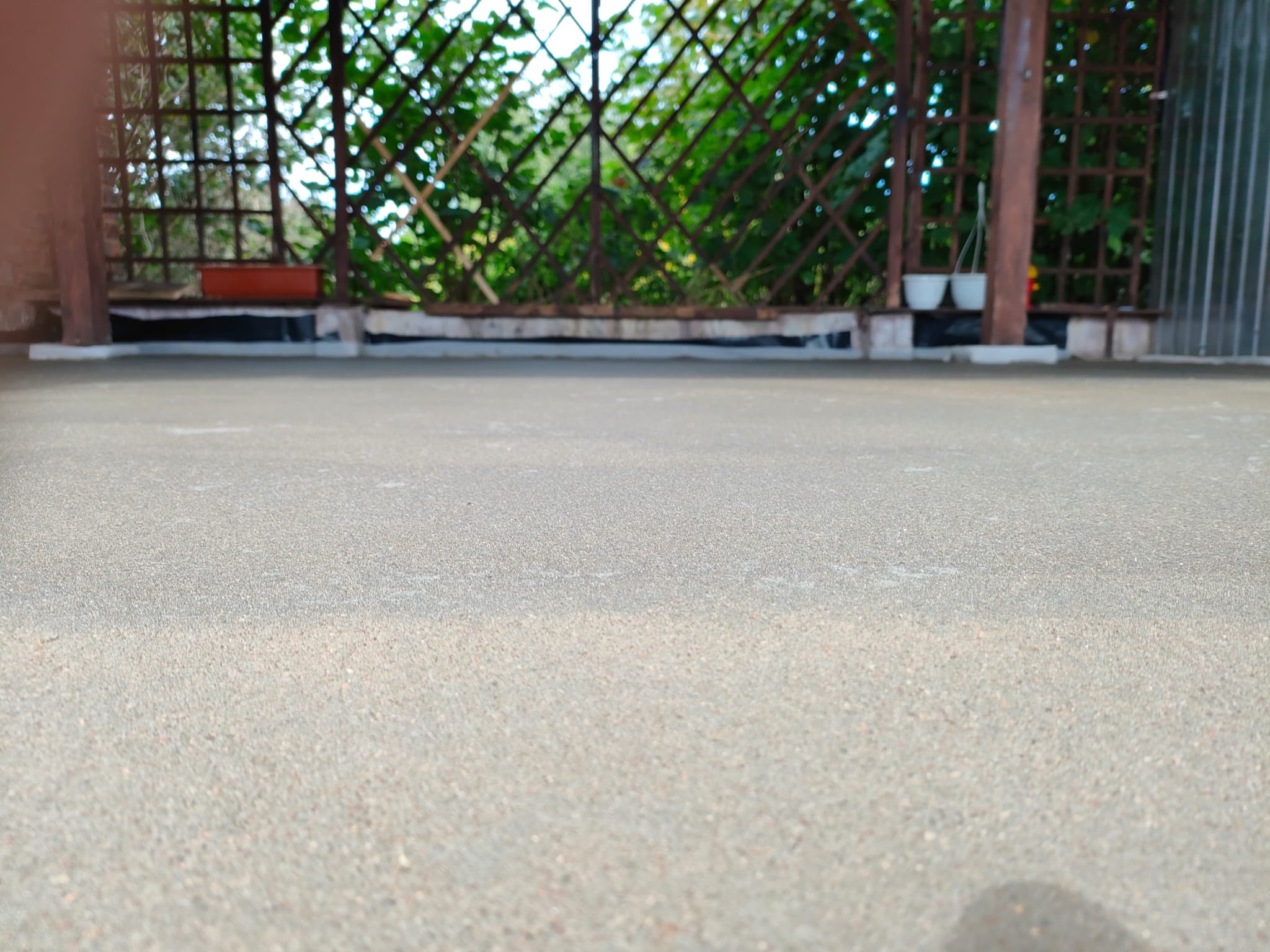 Świeżo wylana, szara posadzka na tarasie z widoczną kratownicą i zielenią w tle, doniczki na krawędzi.