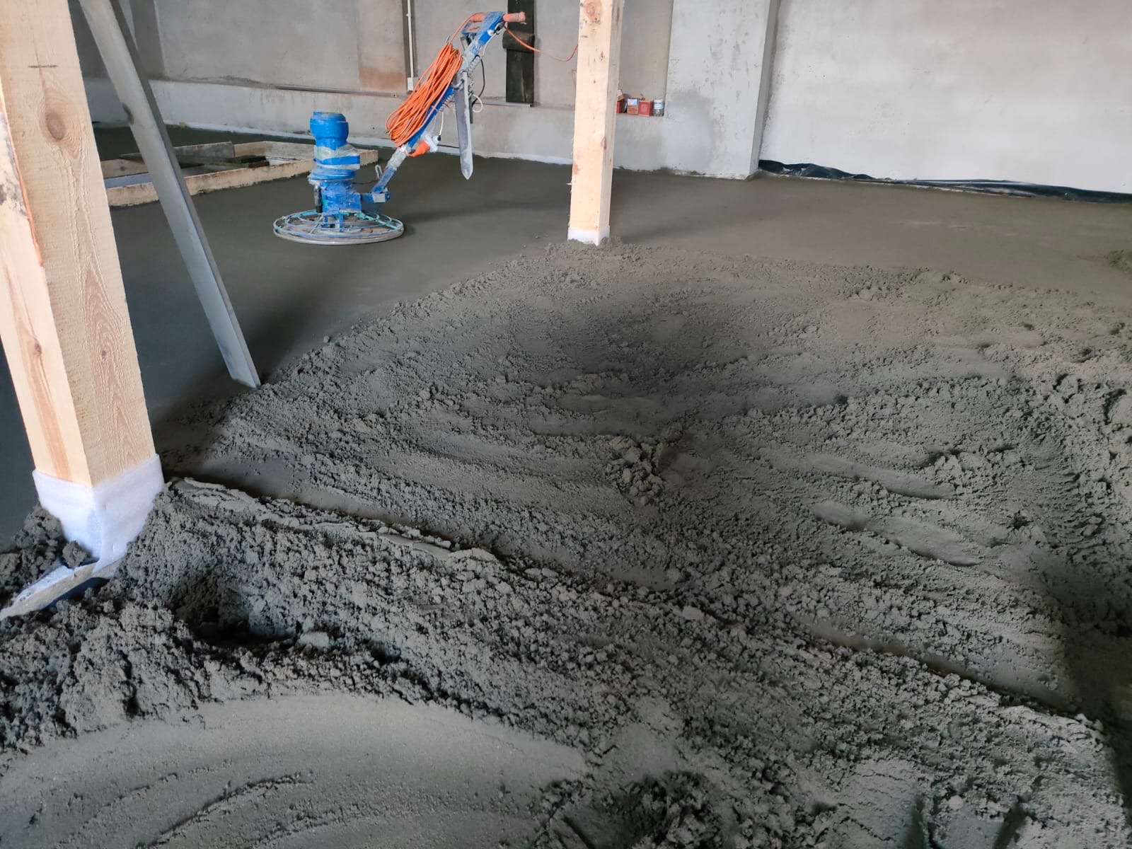 Wylewanie i wyrównywanie posadzki jastrychowej w pomieszczeniu, widoczna maszyna do zacierania, surowy jastrych i drewniane stemple podpierające strop.