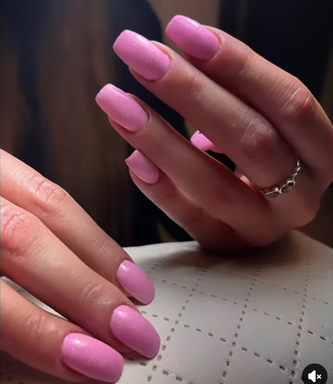 Ręce z kwadratowymi paznokciami pomalowanymi na jasny, błyszczący róż, na poduszce do manicure, z pierścionkiem na palcu.