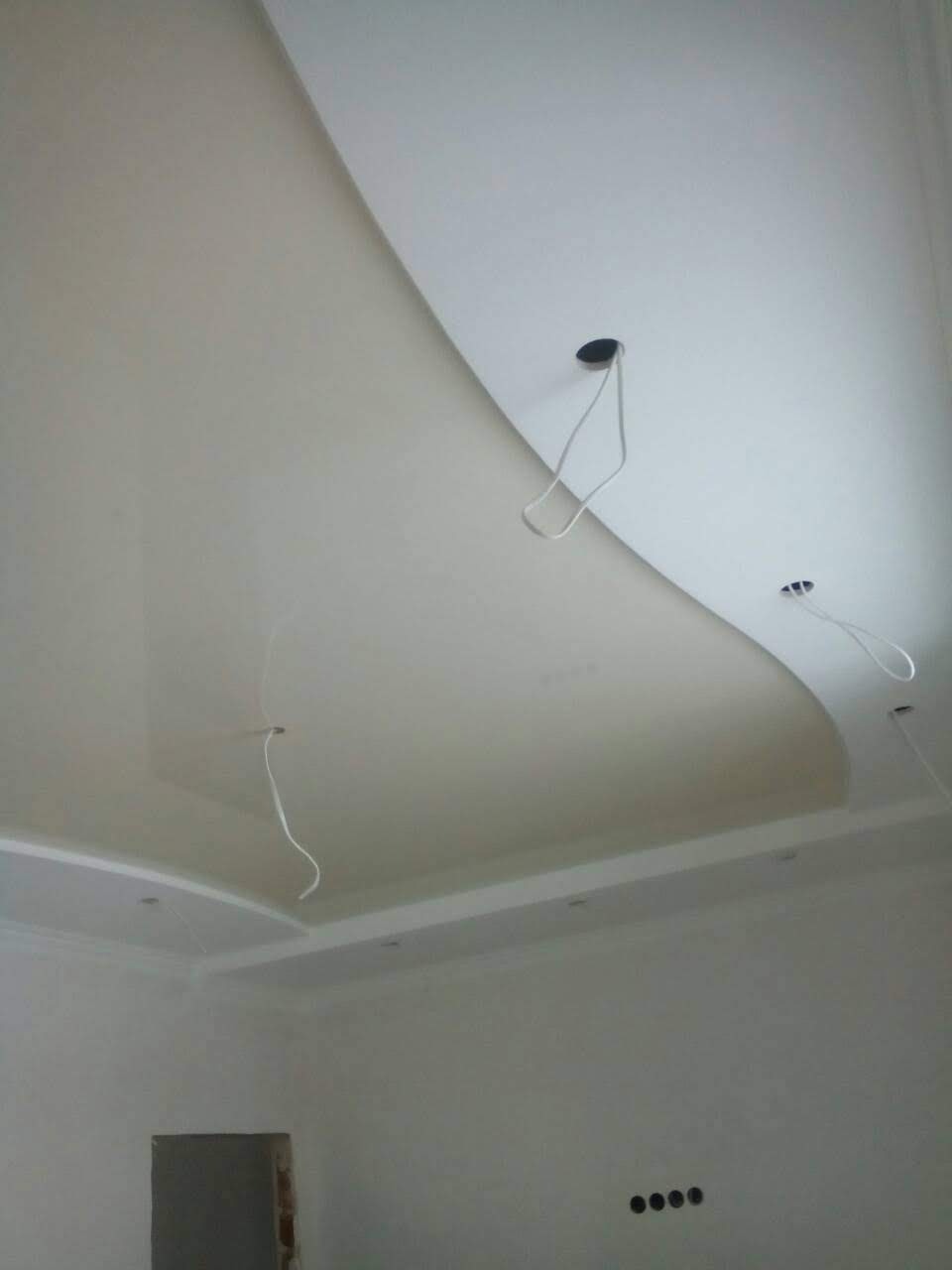 Niedokończony sufit podwieszany z elementami dekoracyjnymi, widoczne kable wystające z otworów pod oświetlenie.