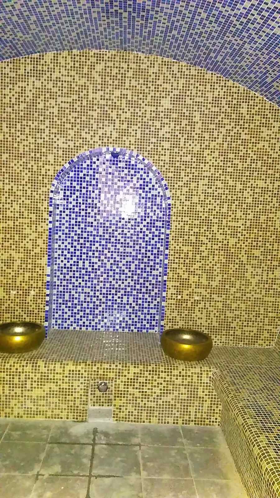 Mozaika z drobnych, kwadratowych płytek w odcieniach złota i błękitu tworząca wnętrze przypominające łaźnię turecką, z dwoma złotymi misami i wnęką z niebieskiej mozaiki.