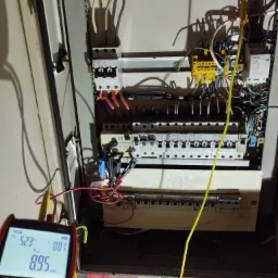 Pomiar rezystancji izolacji w rozdzielnicy elektrycznej za pomocą miernika, widoczne przewody pomiarowe i wyświetlacz urządzenia wskazujący wynik pomiaru w megaomach.