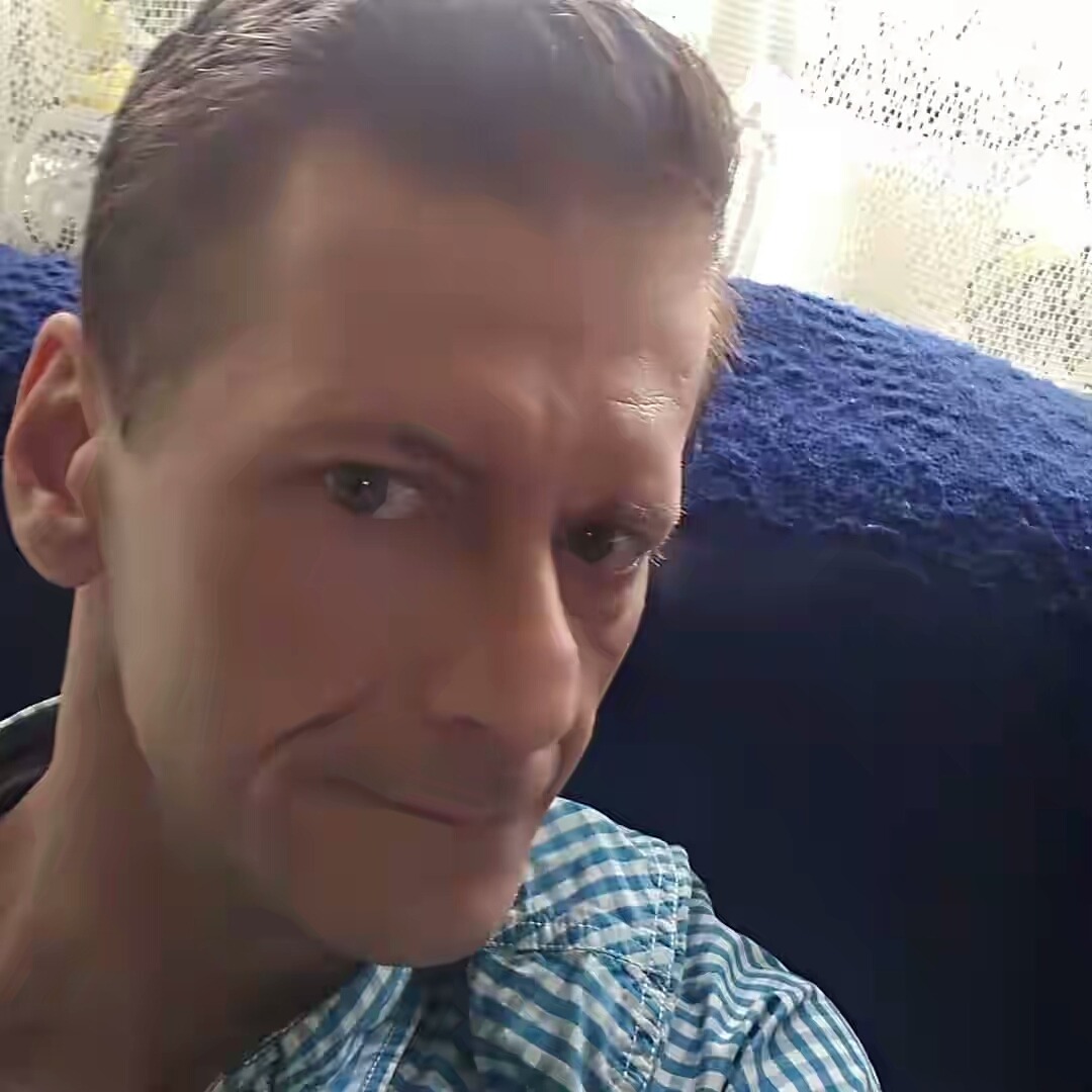 Portret mężczyzny w koszuli w kratę na tle niebieskiej kanapy i białej firanki, zdjęcie z Łodzi.