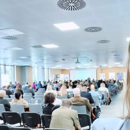 Lokalne Nieruchomości Agnieszka Grzelewska - Sala konferencyjna wypełniona uczestnikami podczas prezentacji. Kobieta w jasnej marynarce robi selfie na tle prelekcji. Widoczny projektor i ekrany.