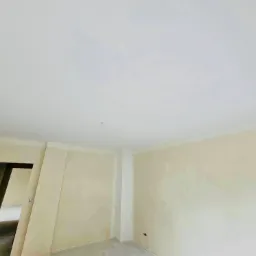 Wnętrze w trakcie prac wykończeniowych, widoczne ściany po szpachlowaniu z widocznymi niedoskonałościami, sufit pomalowany na biało, przygotowanie do malowania.