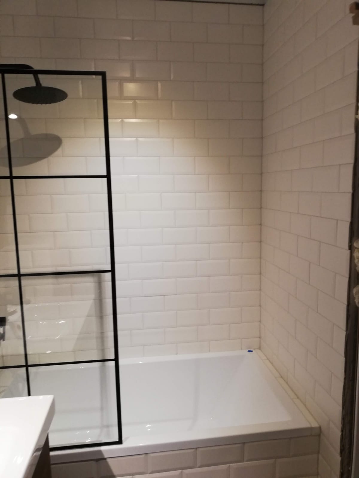 Wykończona łazienka z białą wanną obłożoną płytkami typu metro, czarną kabiną prysznicową i deszczownicą.