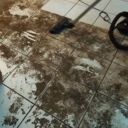 House&Garden K&K Sp z o o - Czyszczenie bardzo zabrudzonej, białej podłogi z płytek ceramicznych za pomocą odkurzacza piorącego. Widoczne ślady czyszczenia i pozostałości brudu.