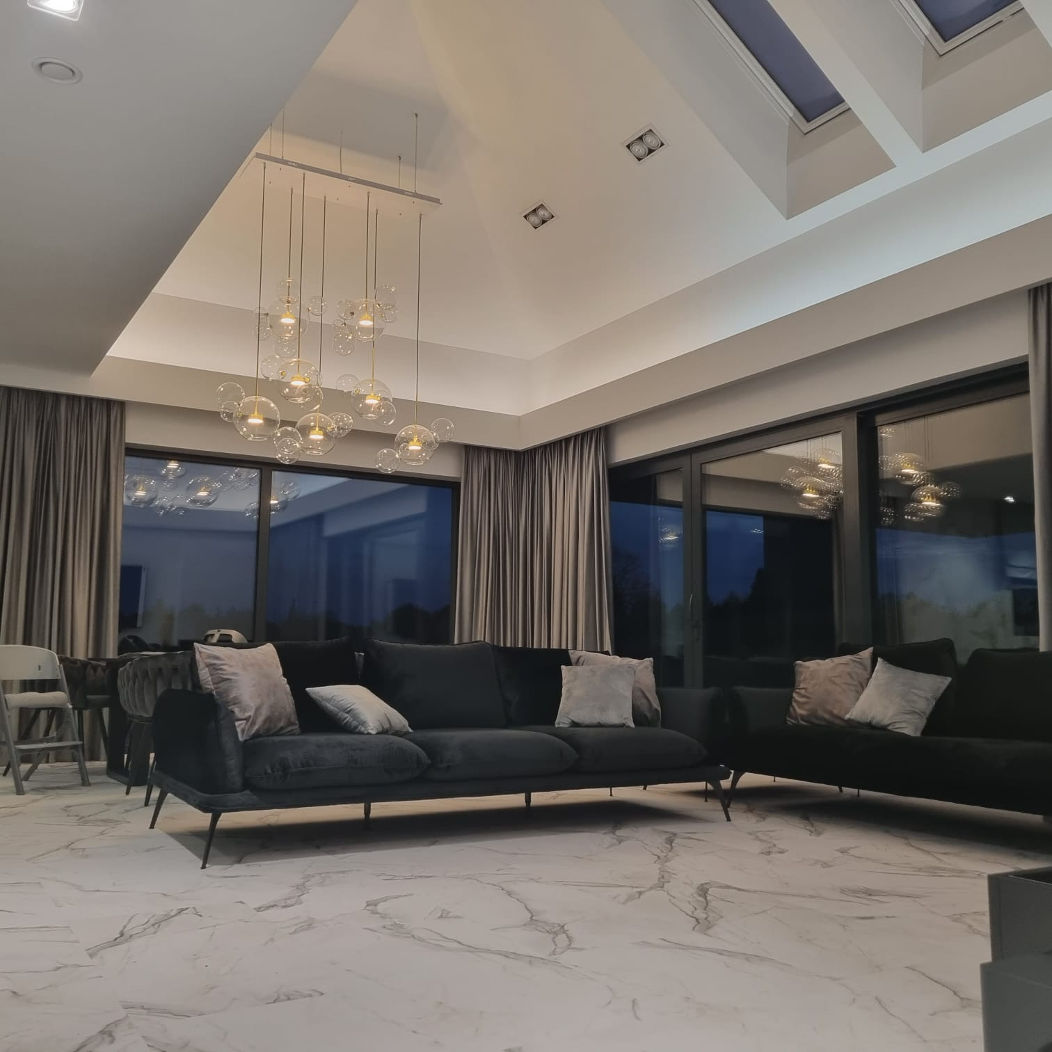 Salon z marmurową posadzką, ciemnymi sofami i nowoczesnym oświetleniem wiszącym.