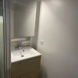 Nowoczesna łazienka z umywalką nablatową na szafce z drewnopodobnym fornirem, lustrem z oświetleniem LED i mozaiką z płytek w odcieniach szarości i beżu.