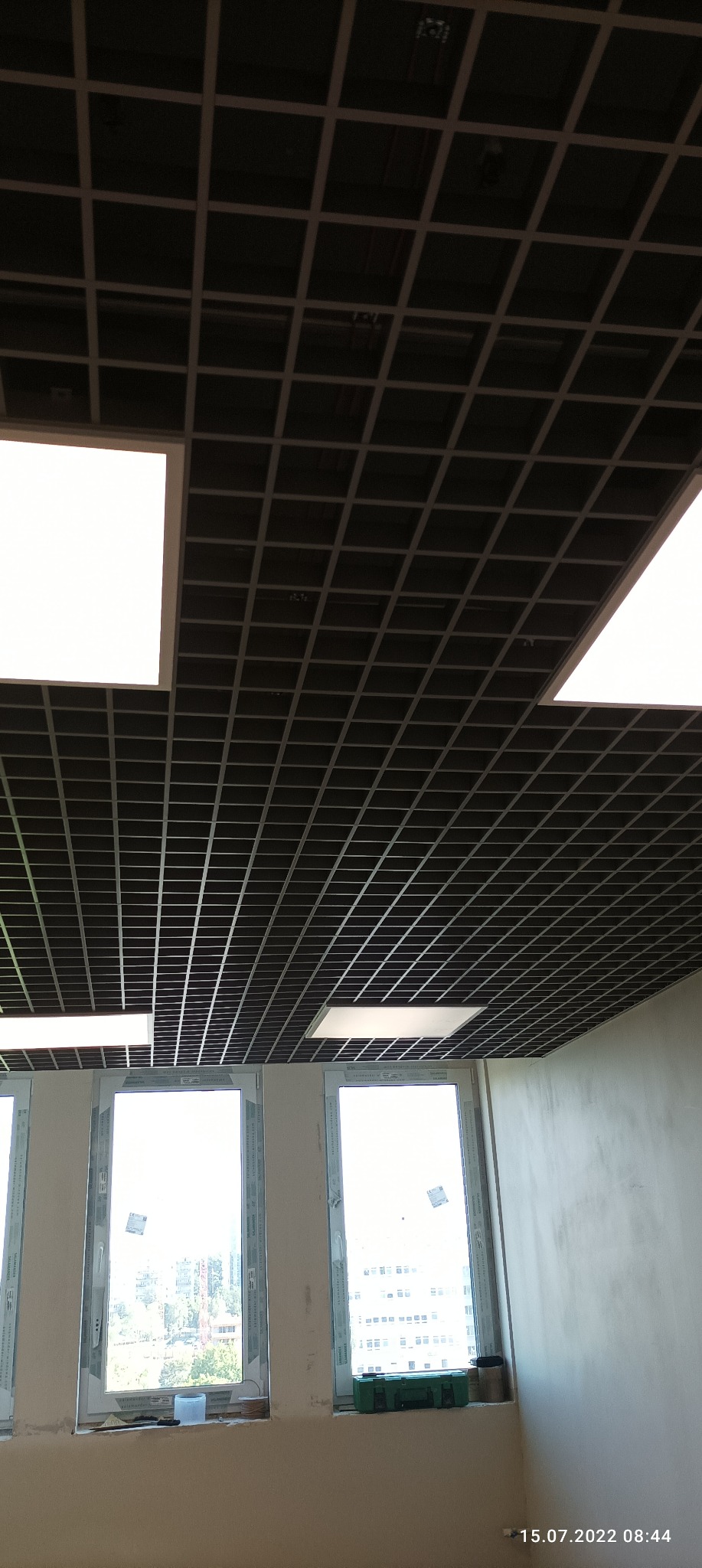 Sufit podwieszany rastrowy z oświetleniem LED w pomieszczeniu z oknami, widok z dołu pod kątem.