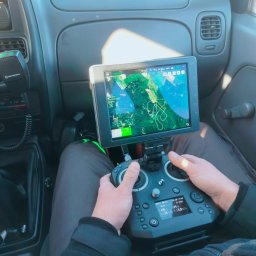 Firma Usługowo- Handlowa Patryk Włoch - Operator drona w kabinie pojazdu, trzymający kontroler z ekranem pokazującym mapę terenu. Motorola CB radio widoczna po lewej stronie.