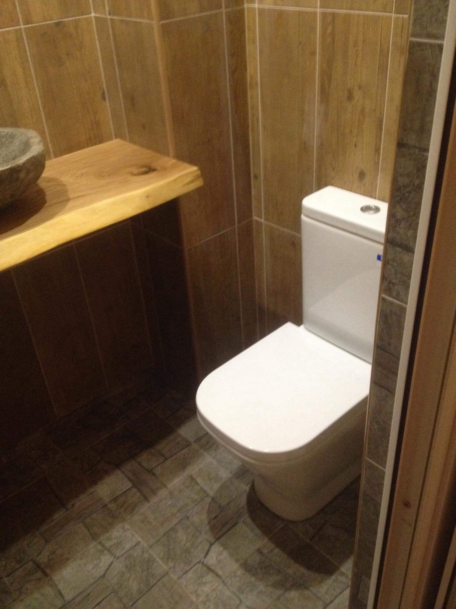 Nowoczesna toaleta z drewnopodobnymi płytkami ściennymi i podłogowymi, kamienna umywalka na blacie z litego drewna.